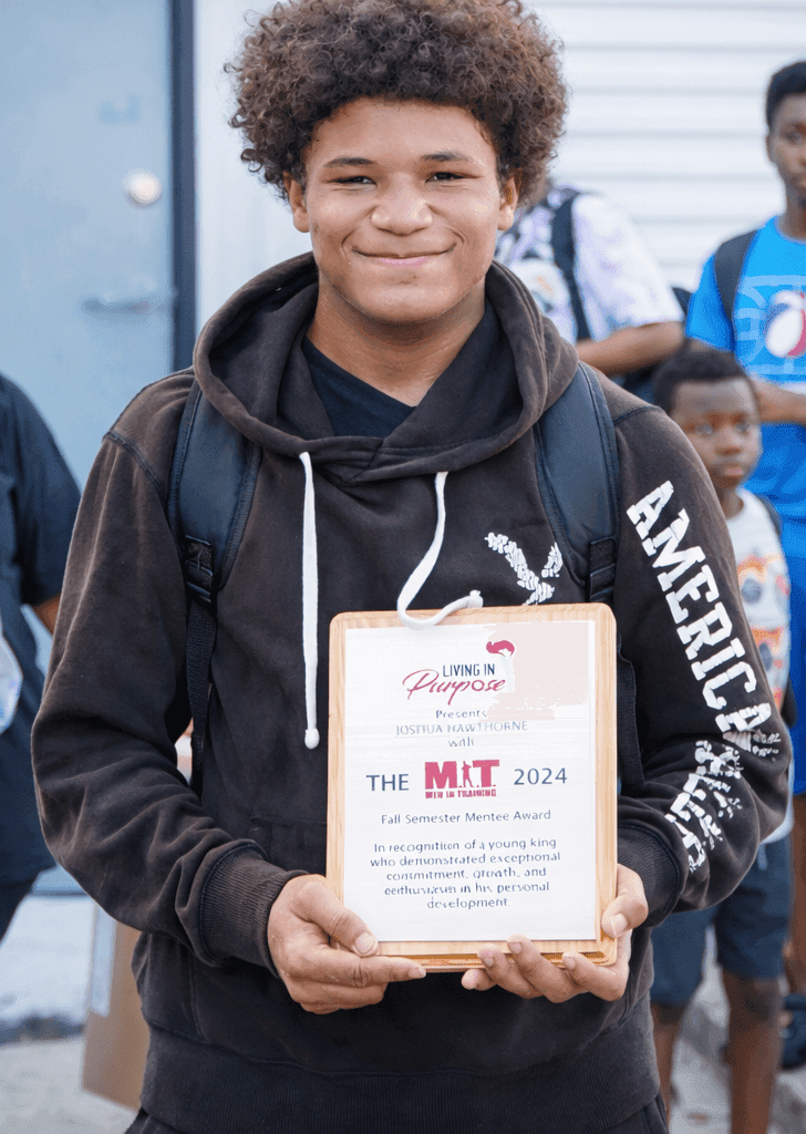 Youth participant holding a mentoring recognition plaque at a Living in Purpose event in Augusta