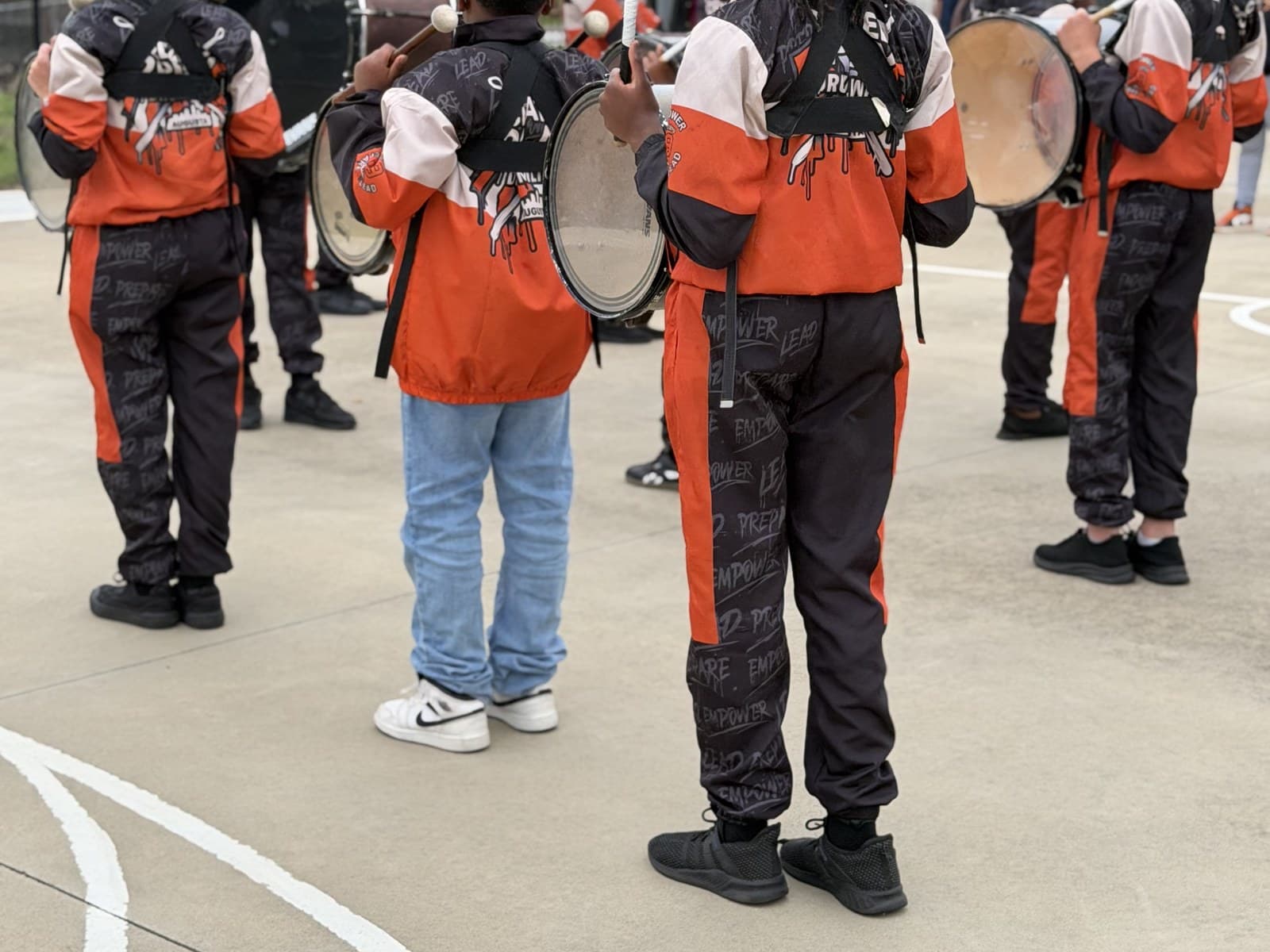 Students in uniform performing as a drumline on an outdoor court